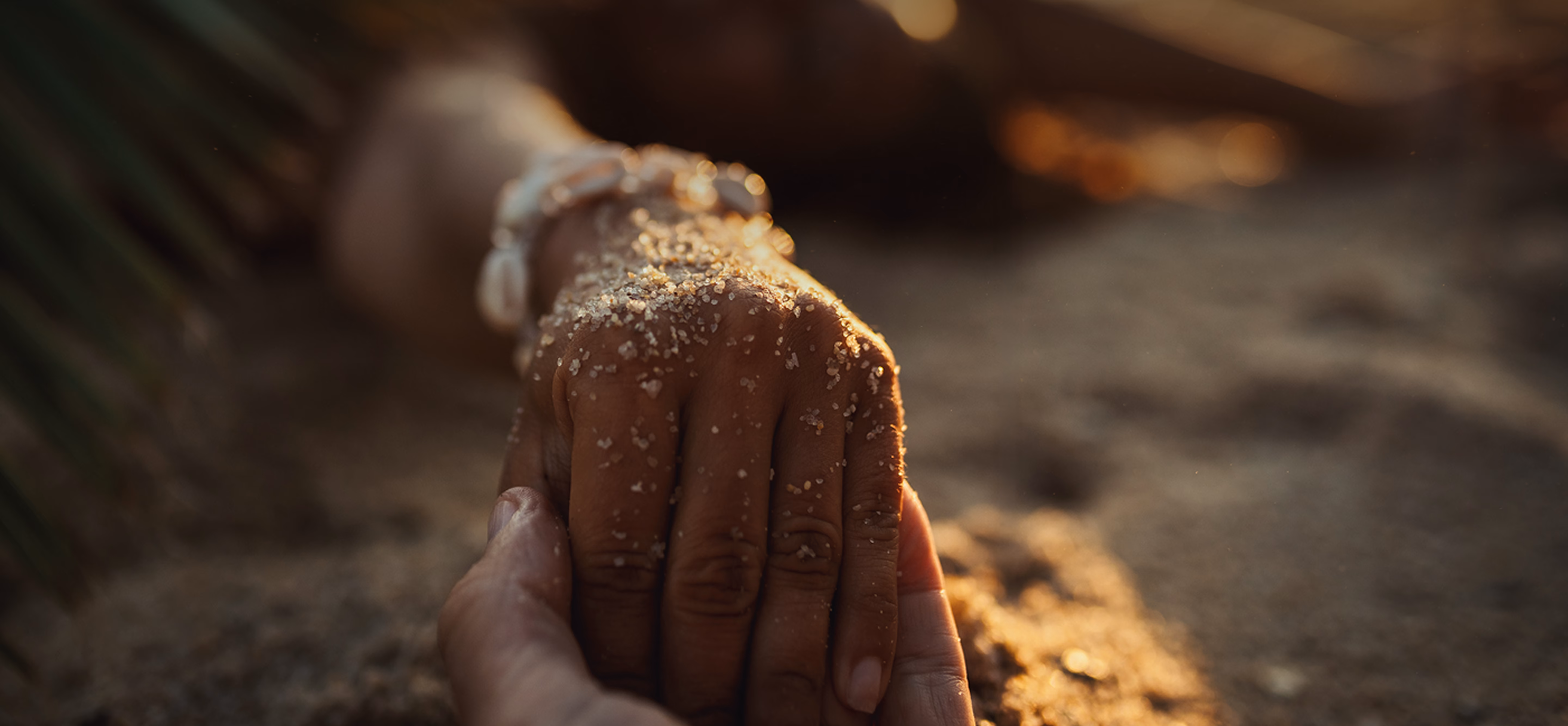 Two hands holding with beach sand in the background